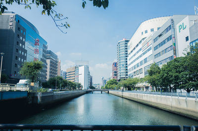 Canal by buildings in city against sky