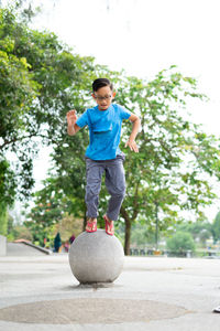 Outdoor portrait of a cute malaysian little boy trying to jump from a concrete ball at the park.