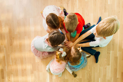 Directly above shot of kids stacking hands while sitting on floor at home