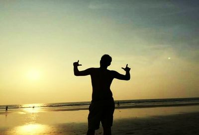 Silhouette man standing at beach against sky during sunset