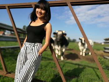 Portrait of happy woman leaning on fence against cows at field