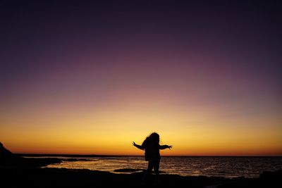 Silhouette person standing on beach against sky during sunset