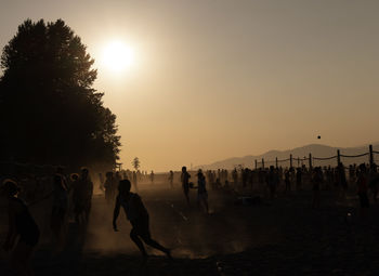 Silhouette people playing volleyball at beach during sunset