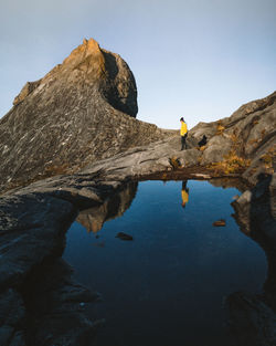 Reflection of woman standing on rock formation in water against sky