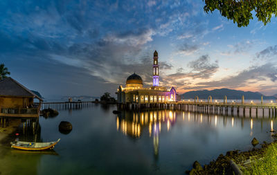 Illuminated building by lake against sky