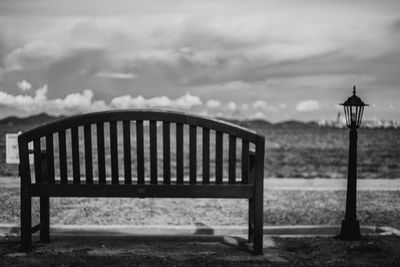 Empty bench on promenade against cloudy sky