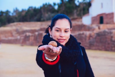 Woman in warm clothing holding stone while standing against built structure