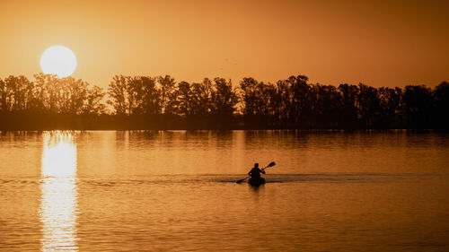 Silhouette person in lake against sky during sunset