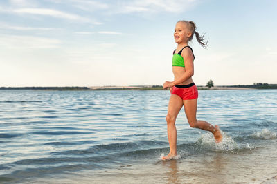 Full length of young woman standing at beach against sky