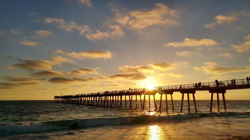 Silhouette people on pier at beach against sky during sunset