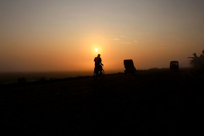 Silhouette people riding on field against sky during sunset