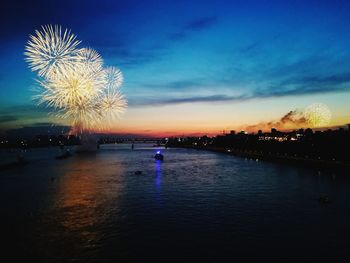 Firework display over river in city against sky