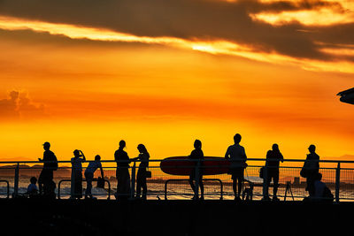 Silhouette people standing by sea against orange sunset sky