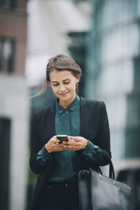 Confident businesswoman text messaging through smart phone while walking in city