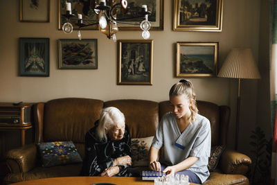 Senior woman and female healthcare worker looking at medicine box in living room