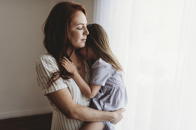 Young mother cuddling with young daughter while closing eyes in studio