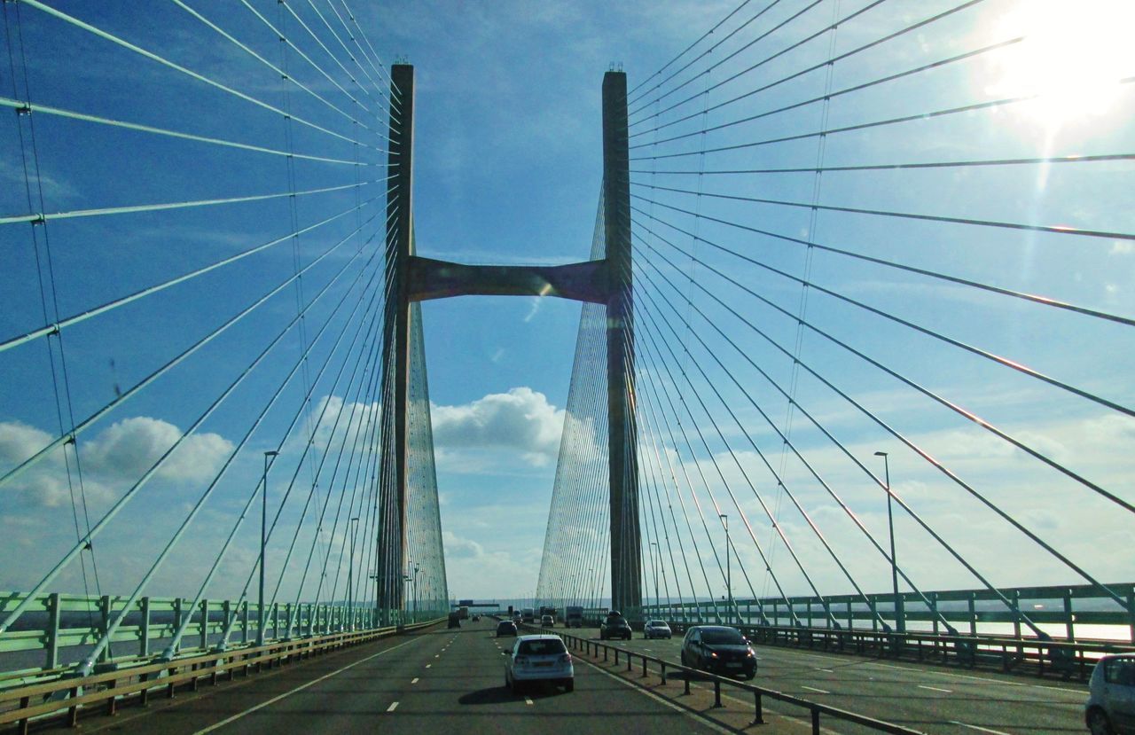 transportation, bridge, cable-stayed bridge, suspension bridge, built structure, architecture, sky, motor vehicle, car, road, mode of transportation, engineering, city, nature, travel, travel destinations, cable, land vehicle, the way forward, steel cable, street, cloud, traffic, highway, day, outdoors, tourism, sunlight, blue, building exterior, sign, city life, line, on the move, motion, symbol, overpass, cityscape, water, diminishing perspective