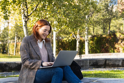 Beautiful business woman with glasses smiling while working on a laptop while sitting in the park.