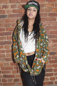 Portrait of young woman standing against brick wall