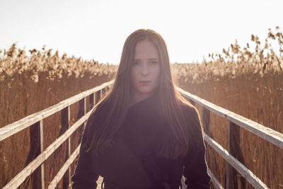 Portrait of young woman standing on boardwalk at farm during sunset