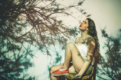 Young woman looking away against trees