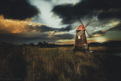 Traditional windmill on field against dramatic sky