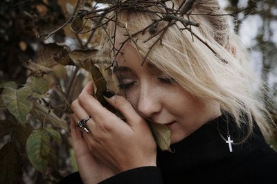 Close-up of beautiful young woman with eyes closed holding branches