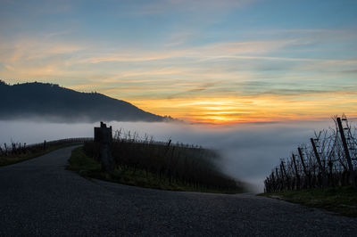 Empty road against cloudy sky at sunset during foggy weather