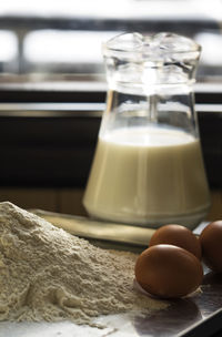 Close-up of flour and eggs by milk in jug on table