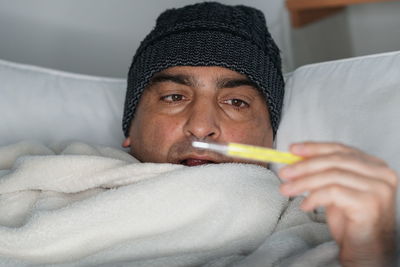 Man checking temperature while lying on bed at home