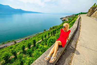 Full length of woman sitting by road against lake