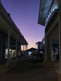 Illuminated street amidst buildings against sky at sunset