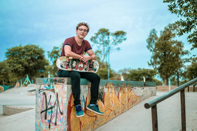 Portrait of young man sitting on railing against trees