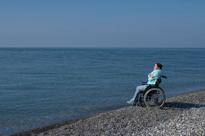 Rear view of man riding bicycle on beach against clear sky