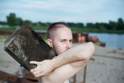 Portrait of young man holding sunglasses against lake