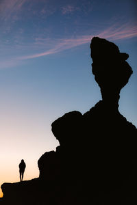 Silhouette man standing on rock against sky during sunset