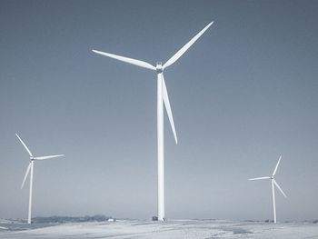 Wind turbines on snow covered landscape against clear sky