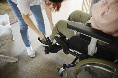 Mother helping disabled daughter in wheelchair putting her shoes on