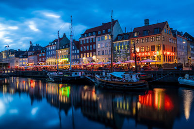 River by illuminated buildings against sky at dusk