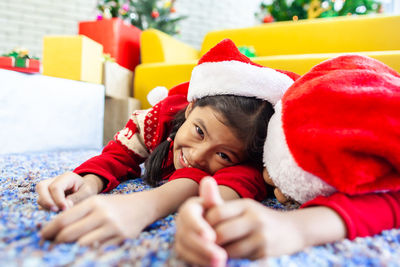 Portrait of cute girl lying with sister on rug during christmas