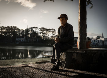 Full length of senior man looking away while sitting in park during sunset