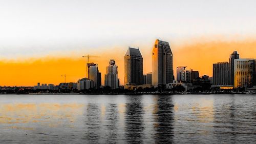 Sea by cityscape against sky during sunset