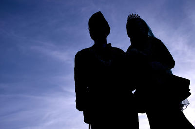 Low angle view of silhouette couple standing against sky