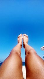 Low section of woman feet up against clear blue sky