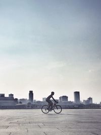 Man riding bicycle on street in city against sky