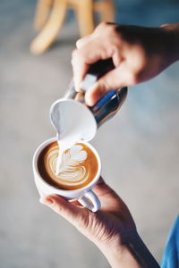 Close-up of hand making froth art in coffee