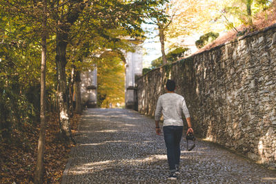 Rear view of woman walking on road along trees