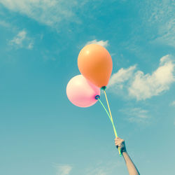 Low angle view of hand holding balloons against sky