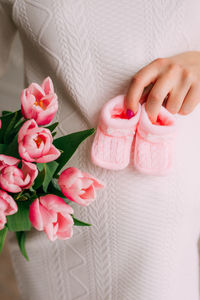 Midsection of woman holding rose bouquet with baby booties