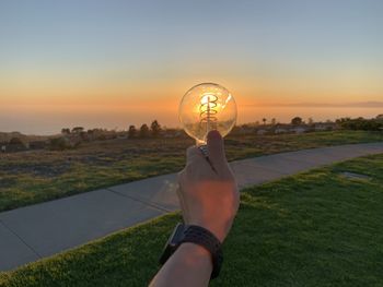Man holding umbrella on field against sky during sunset